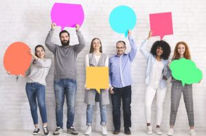 Symbolising having cooperative conversations in order to increase workplace inclusivity and diversity, this photo is of men and women of all ages and colours holding different shaped speech bubbles